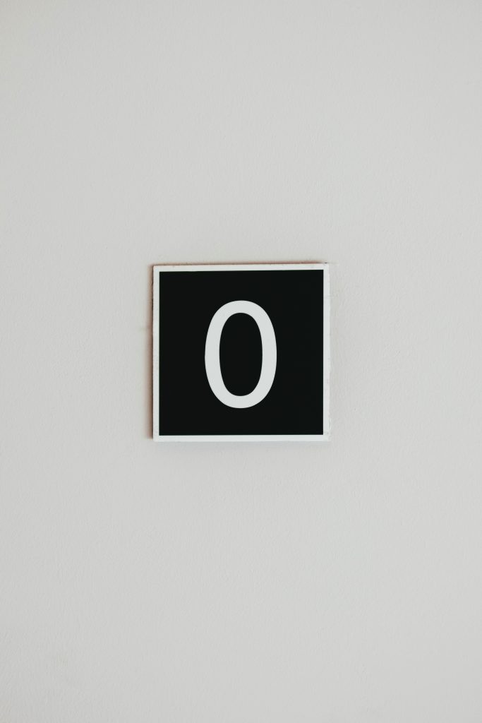 A small black sign on a white wall showing the numeral zero.